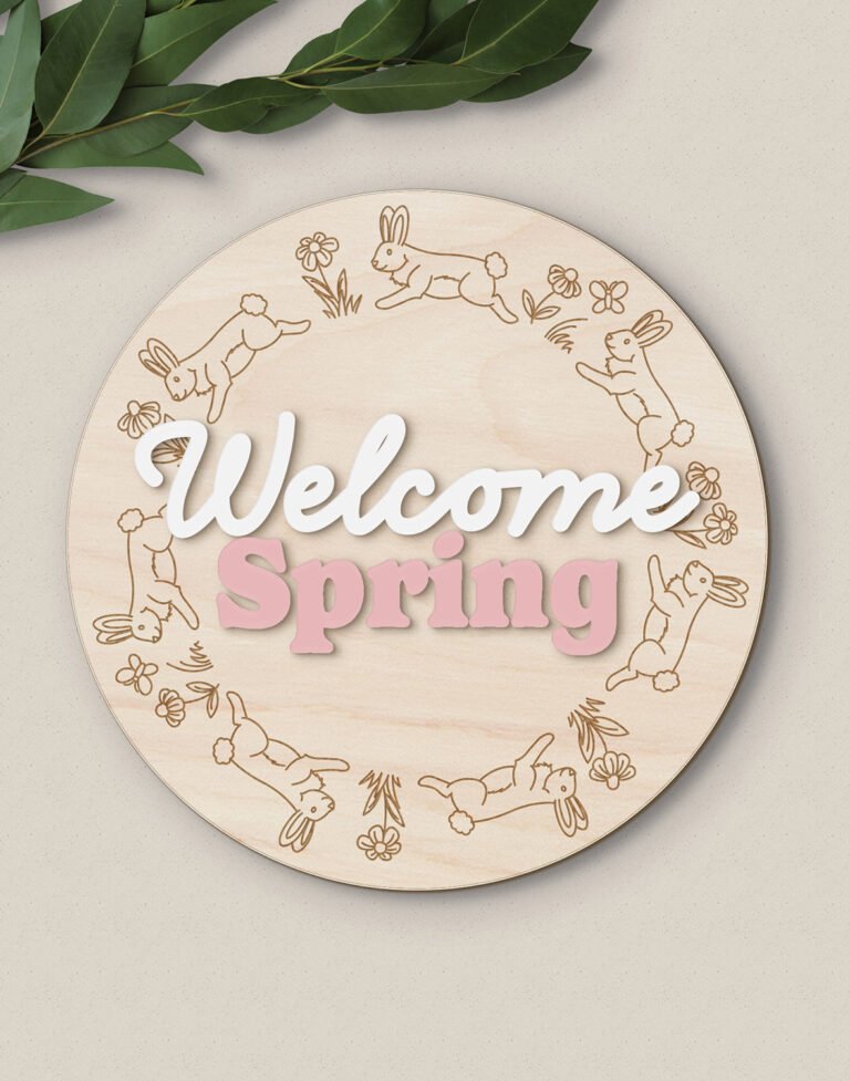 a round wooden sign featuring the words "Welcome Spring" with an engraved border of hopping bunnies, flowers and butterflies - a laser SVG file designed by ShopSarahRenee